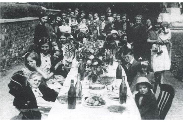 Black and whire photo. VE Day street party in Llandaff. Children and adults around a large table of food and drink.